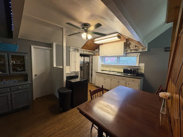 kitchen with dark countertops, vaulted ceiling, wood finished floors, a sink, and stainless steel microwave
