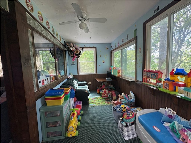 playroom with carpet flooring, a ceiling fan, a wainscoted wall, and wooden walls