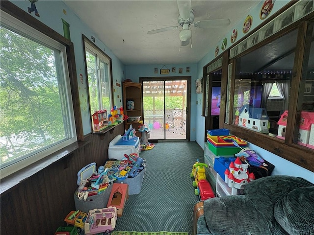 game room featuring carpet floors, a wainscoted wall, a ceiling fan, and wood walls