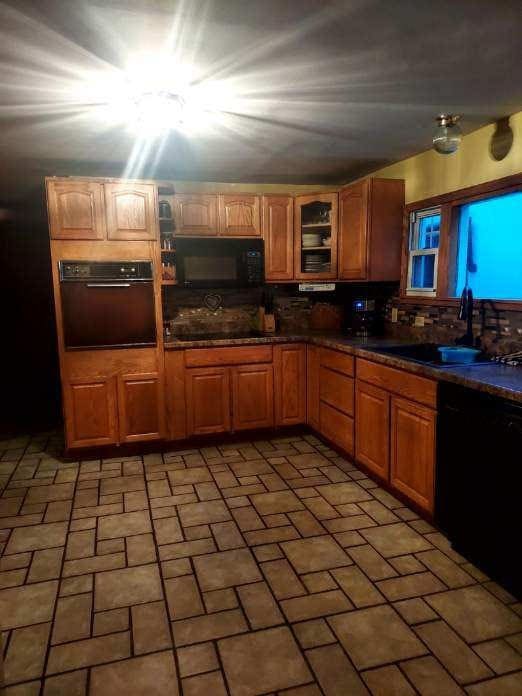 kitchen featuring glass insert cabinets, dark countertops, brick floor, and black appliances