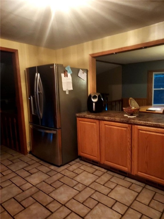 kitchen featuring stainless steel fridge, brick floor, and dark countertops