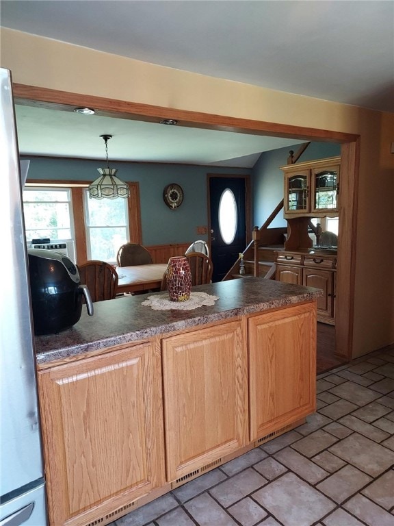 kitchen with freestanding refrigerator, dark countertops, pendant lighting, and brick floor