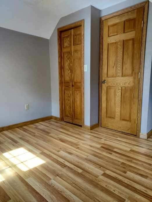 unfurnished bedroom with a closet, baseboards, lofted ceiling, and light wood-type flooring