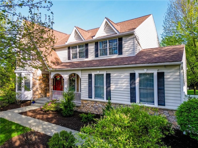 traditional-style home featuring a porch, roof with shingles, and stone siding