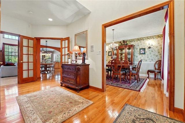 corridor with arched walkways, an inviting chandelier, french doors, and hardwood / wood-style floors