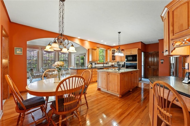 kitchen with light wood-style floors, a chandelier, recessed lighting, a center island with sink, and black appliances