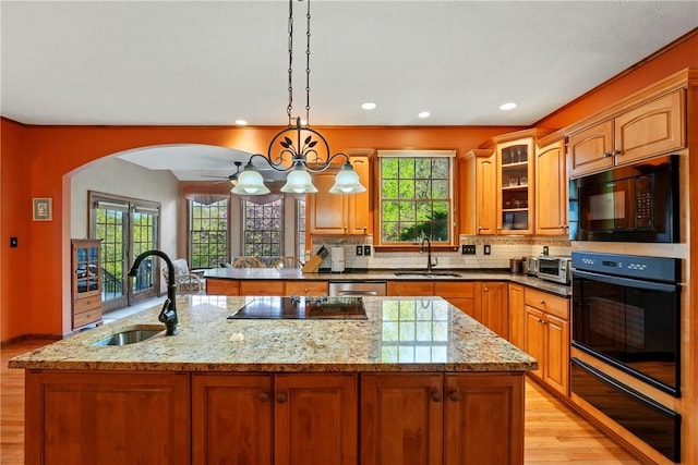kitchen featuring light wood-type flooring, a sink, black appliances, and light stone countertops