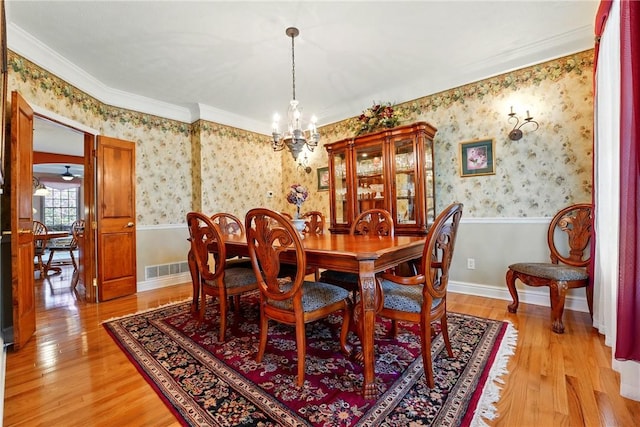dining space with an inviting chandelier, ornamental molding, wainscoting, light wood-style floors, and wallpapered walls