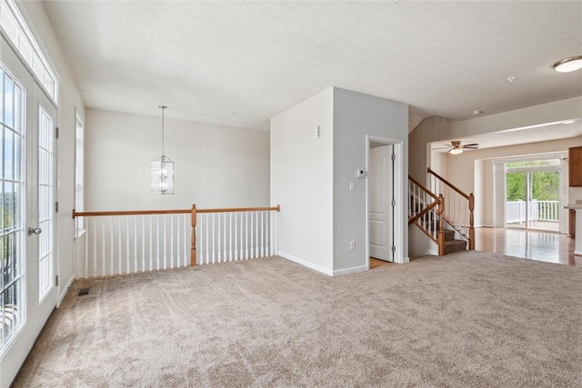 carpeted spare room with baseboards, ceiling fan with notable chandelier, visible vents, and stairway
