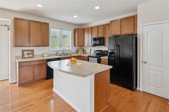 kitchen with a kitchen island, light countertops, a sink, light wood-style flooring, and black appliances