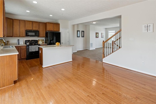 kitchen featuring a sink, light countertops, light wood-style flooring, a center island, and black appliances