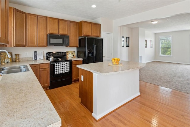kitchen with brown cabinets, a sink, light countertops, black appliances, and open floor plan
