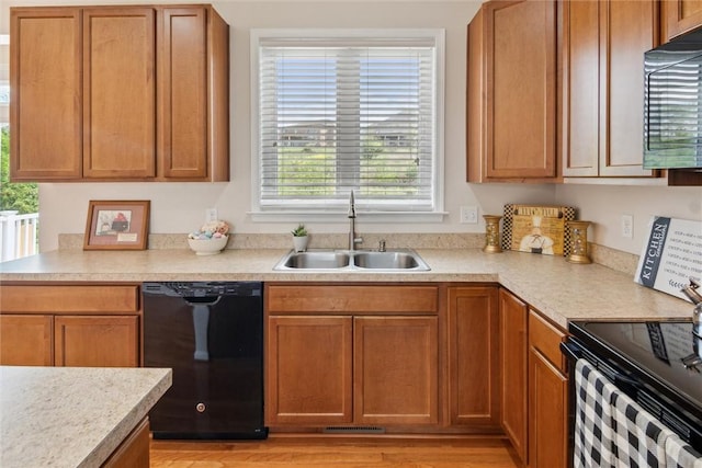 kitchen featuring light countertops, a sink, black appliances, and light wood-type flooring