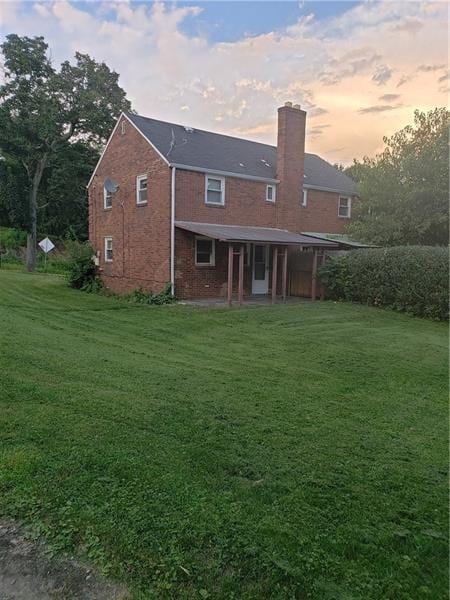 back of property at dusk with a yard, brick siding, and a chimney