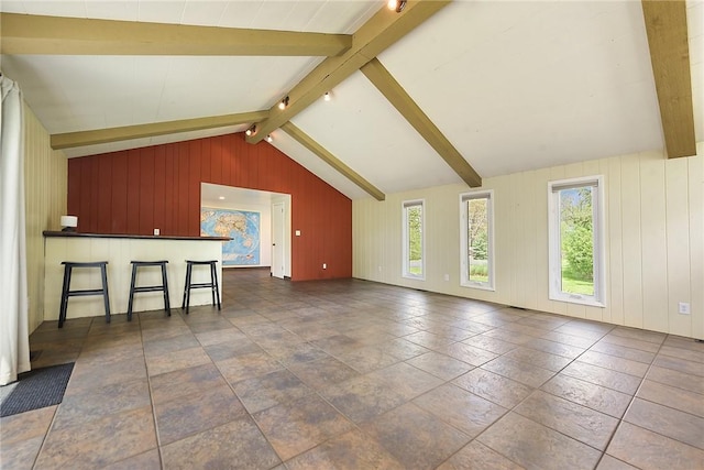 unfurnished living room with plenty of natural light, lofted ceiling with beams, and wooden walls