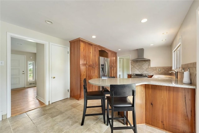 kitchen with wall chimney range hood, appliances with stainless steel finishes, tasteful backsplash, a sink, and a peninsula