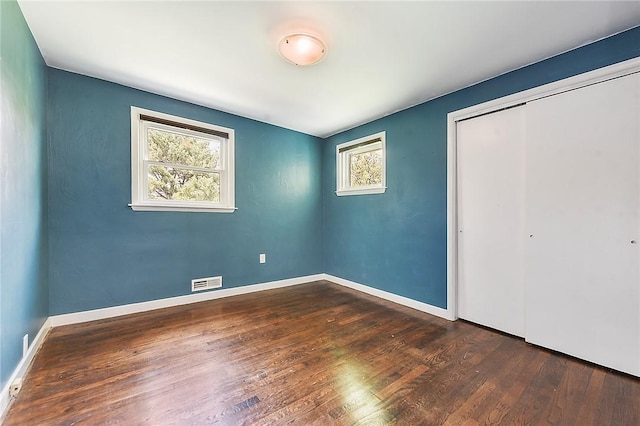 unfurnished bedroom featuring dark wood-style floors, visible vents, multiple windows, and a closet
