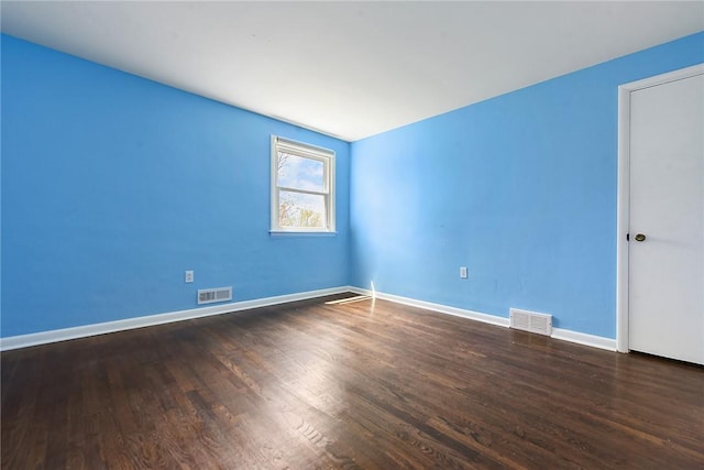 empty room featuring baseboards, wood finished floors, and visible vents