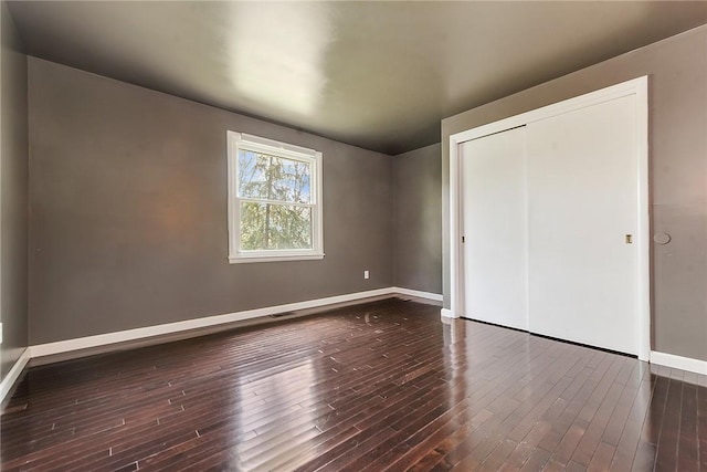 unfurnished bedroom featuring baseboards, dark wood-type flooring, visible vents, and a closet