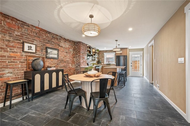 dining area featuring baseboards, stone tile flooring, and brick wall