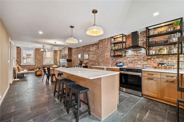 kitchen with stainless steel electric range, wall chimney range hood, brick wall, a kitchen breakfast bar, and pendant lighting
