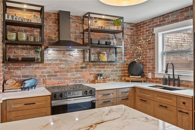 kitchen featuring wall chimney range hood, stainless steel range with electric cooktop, a sink, and light stone counters