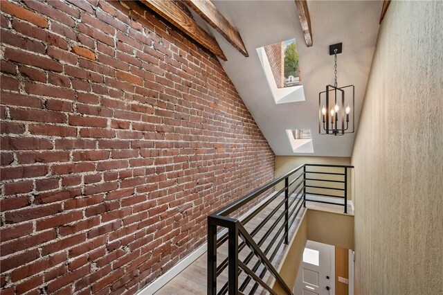 stairway with a skylight, a chandelier, wood finished floors, and brick wall