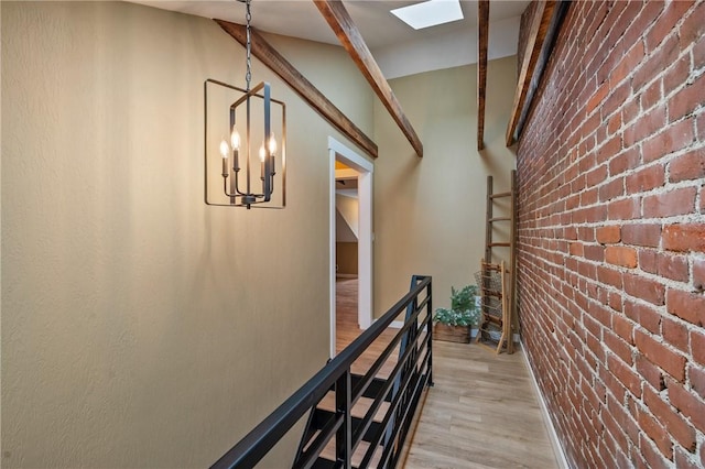 corridor featuring light wood-style flooring, brick wall, a chandelier, and a skylight