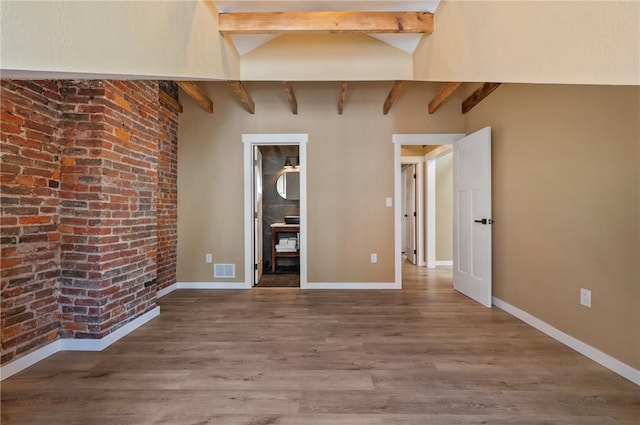 empty room featuring beamed ceiling, wood finished floors, brick wall, and baseboards