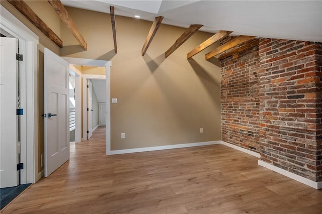 basement featuring brick wall, baseboards, and light wood-type flooring