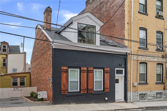 view of front facade featuring brick siding, cooling unit, a chimney, and fence