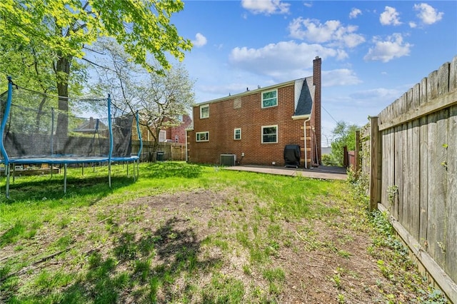back of property featuring a chimney, a trampoline, a fenced backyard, a yard, and a patio