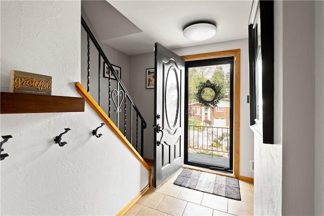 foyer with baseboards, a textured wall, light tile patterned floors, and stairway