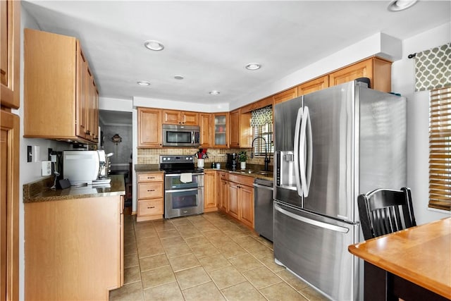 kitchen featuring light tile patterned flooring, a sink, stainless steel appliances, decorative backsplash, and glass insert cabinets