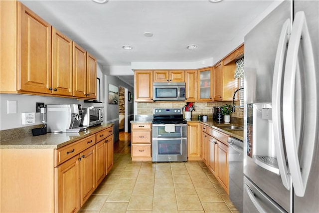 kitchen featuring appliances with stainless steel finishes, a sink, decorative backsplash, light tile patterned floors, and glass insert cabinets