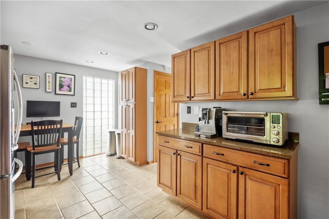 kitchen with a toaster, dark stone countertops, freestanding refrigerator, and brown cabinets