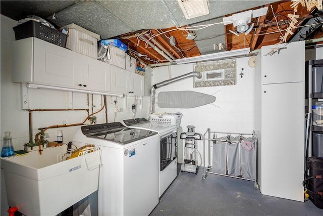 clothes washing area featuring a sink, concrete block wall, cabinet space, and independent washer and dryer