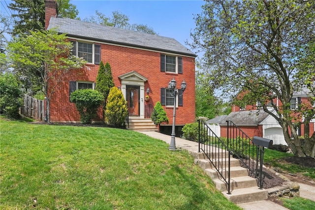 colonial inspired home featuring brick siding, fence, a chimney, and a front yard