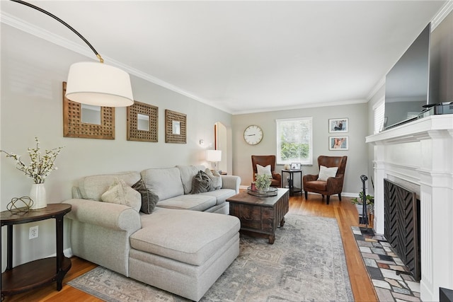 living room with crown molding, a fireplace with flush hearth, baseboards, and wood finished floors