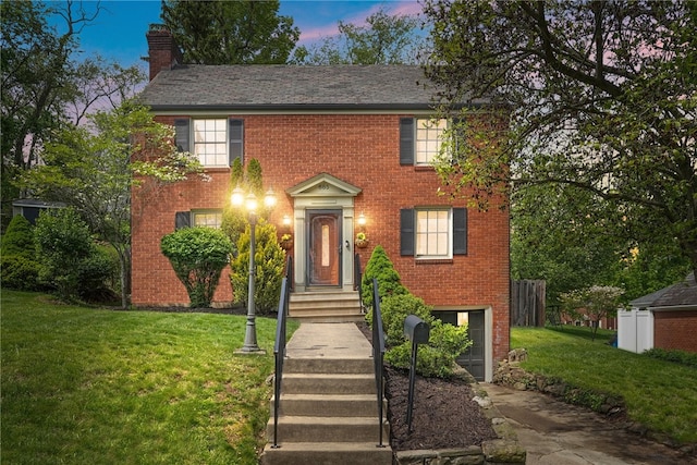 colonial home featuring brick siding, fence, a chimney, and a front yard