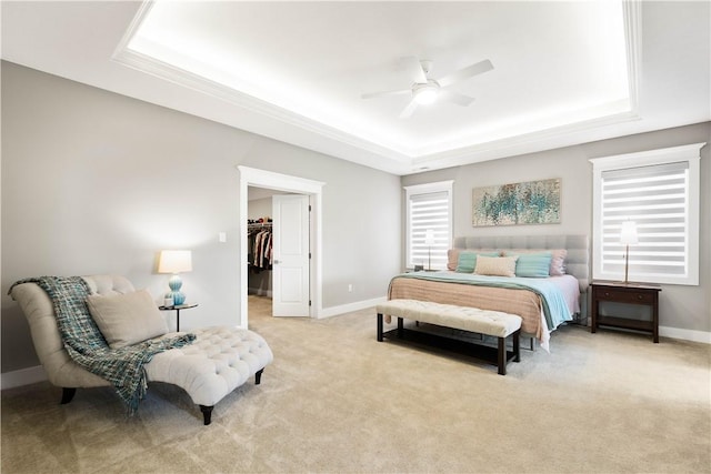 bedroom with a closet, light carpet, baseboards, a walk in closet, and a raised ceiling