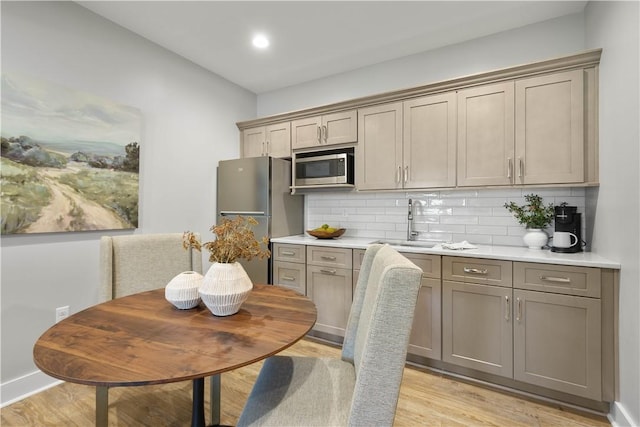 kitchen with backsplash, appliances with stainless steel finishes, a sink, and light wood-style floors