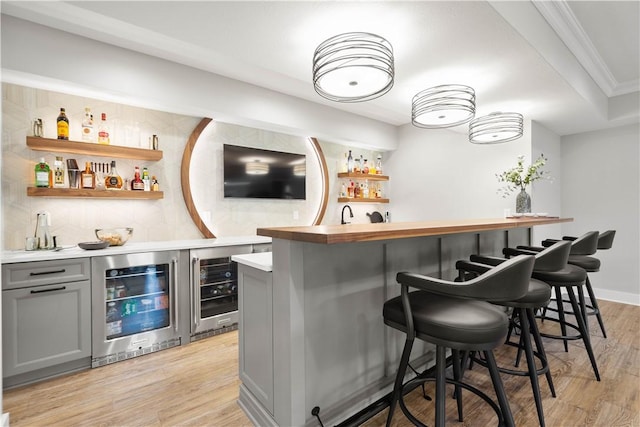 bar with indoor wet bar, crown molding, light wood-style floors, and wine cooler