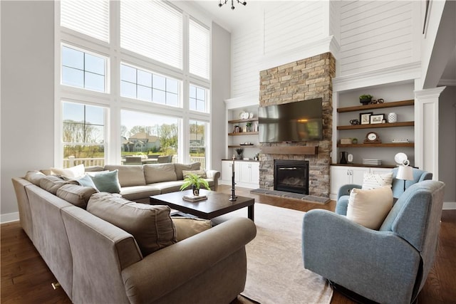 living room with built in features, a fireplace, baseboards, a high ceiling, and dark wood-style floors