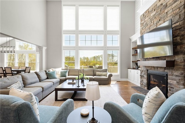 living room with a high ceiling, a healthy amount of sunlight, wood finished floors, and a stone fireplace