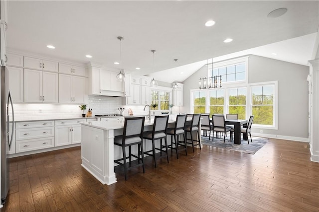 kitchen with a kitchen breakfast bar, a kitchen island with sink, vaulted ceiling, white cabinetry, and dark wood-type flooring