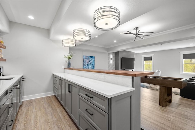 kitchen featuring light wood-style floors, ornamental molding, a peninsula, and gray cabinetry