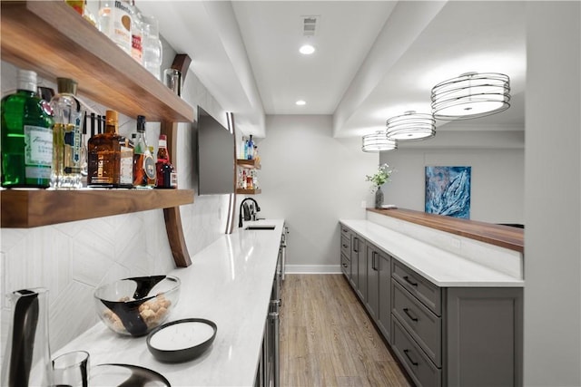 bar featuring visible vents, a sink, baseboards, light wood finished floors, and recessed lighting