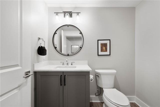 half bath with toilet, baseboards, wood finished floors, and vanity