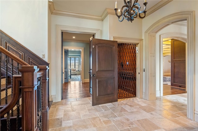wine room featuring arched walkways, baseboards, an inviting chandelier, ornamental molding, and stone tile floors